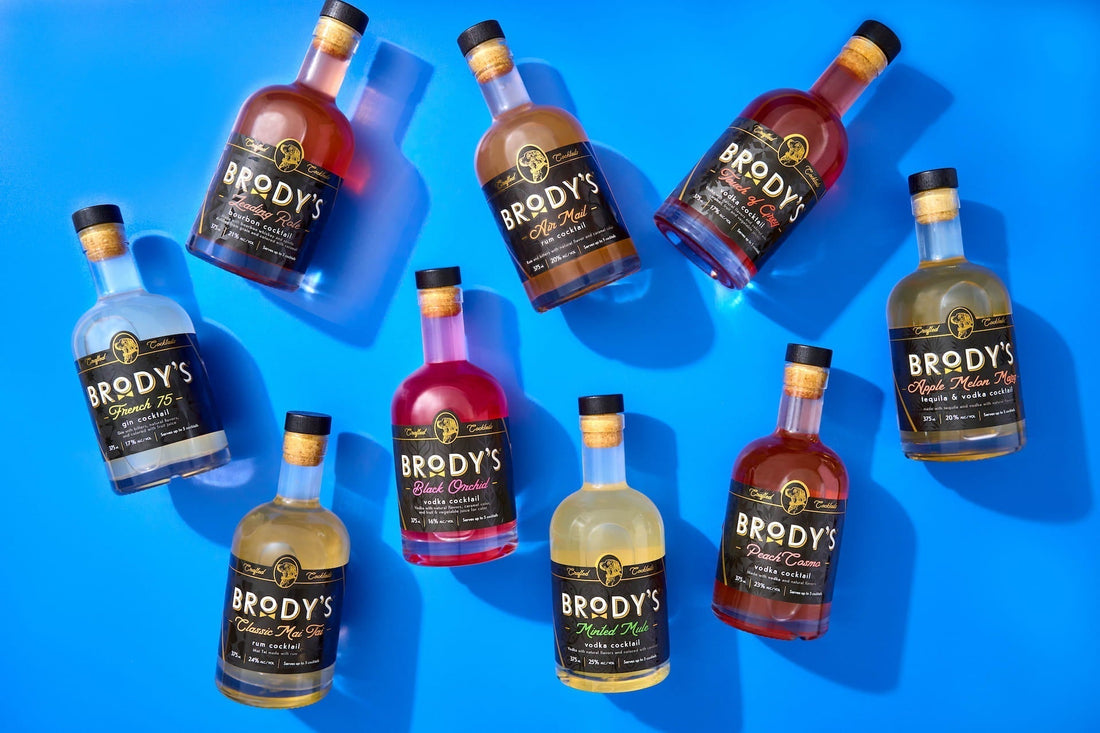 Nine Brody's Crafted Cocktails bottles arranged overhead for a dinner party spread — premixed cocktails for entertaining