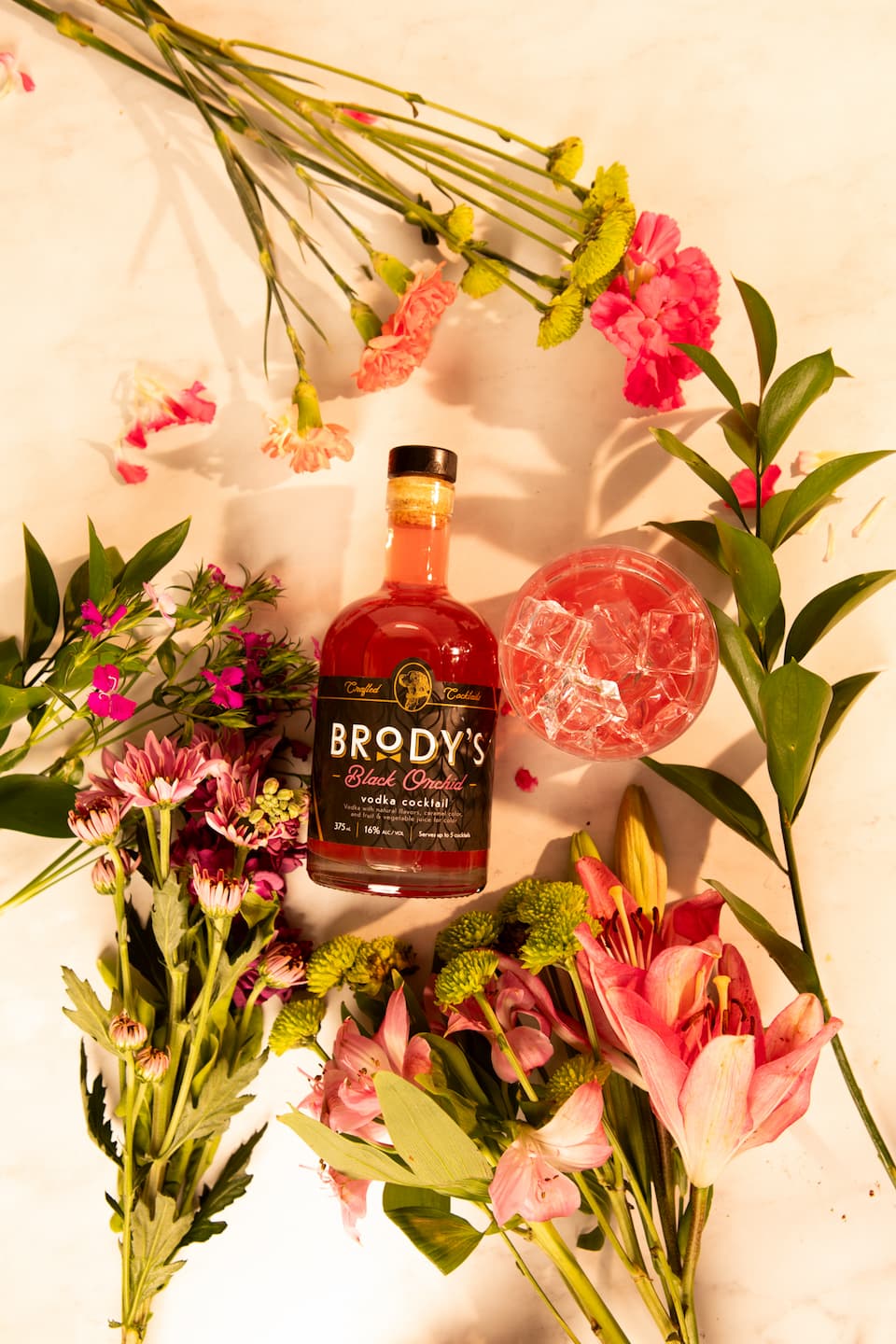 A bottle of Brody's Black Orchid cocktail surrounded by pink florals and dark foliage.