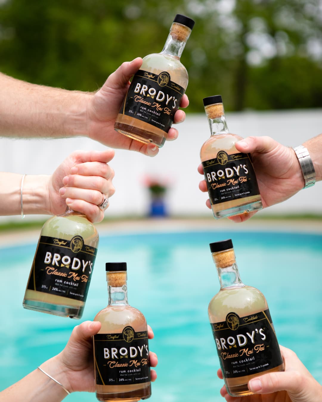 Friends toasting with Brody's Classic Mai Tai rum cocktail bottles by the pool