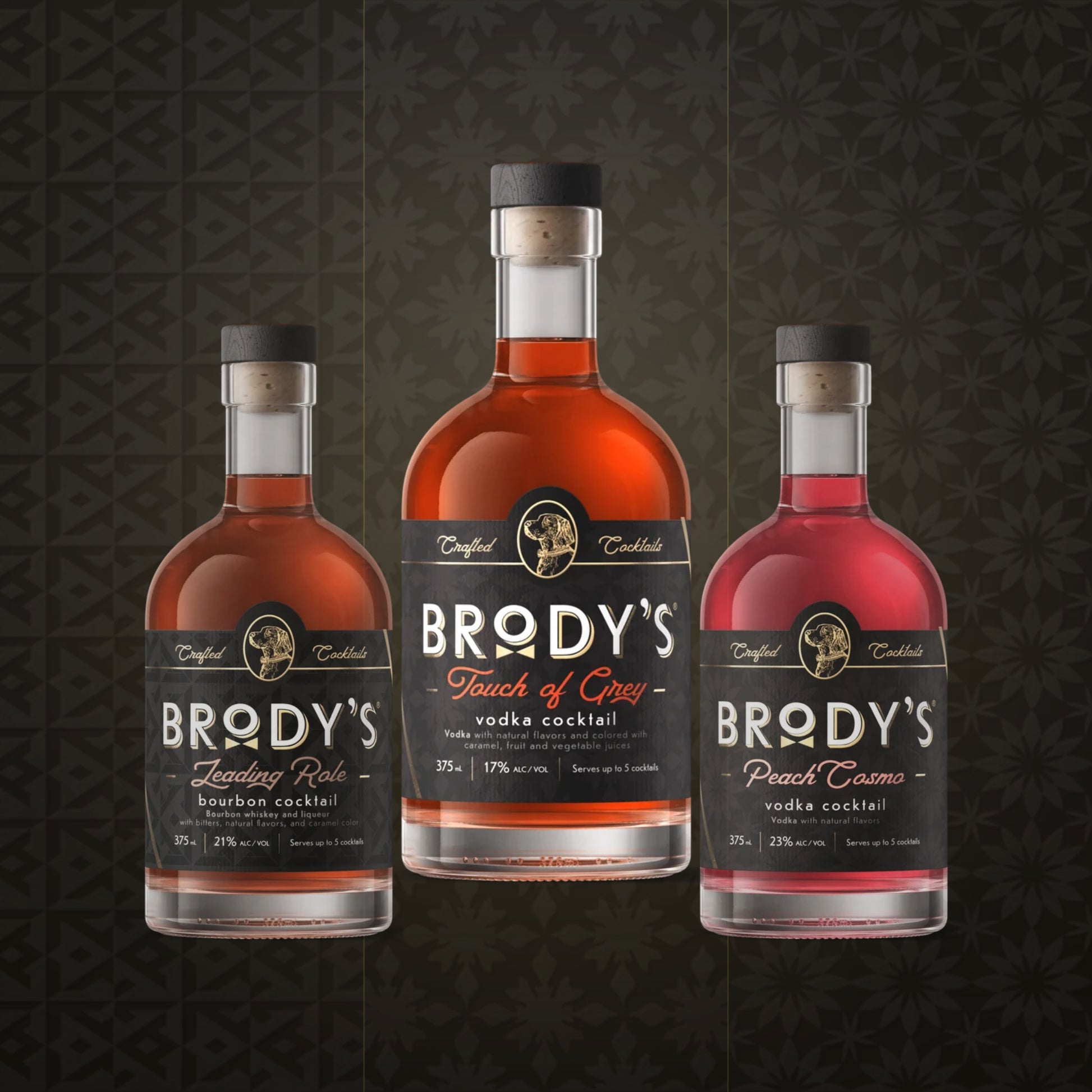 Three bottles of Brody's Cocktail mix displayed against a dark patterned background. The center bottle is 'Touch of Grey' vodka cocktail, flanked by 'Leading Role' bourbon cocktail on the left and 'Peach Cosmo' vodka cocktail on the right.