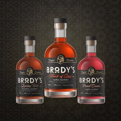 Three bottles of Brody's Cocktail mix displayed against a dark patterned background. The center bottle is 'Touch of Grey' vodka cocktail, flanked by 'Leading Role' bourbon cocktail on the left and 'Peach Cosmo' vodka cocktail on the right.